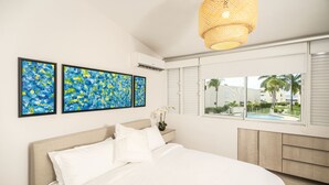 A modern bedroom with a large bed, white bedding, and three abstract paintings on the wall. - Dream Villa · Direct Beach Access · Pool · 2BR Gated · Dorado, PR (Dorado)