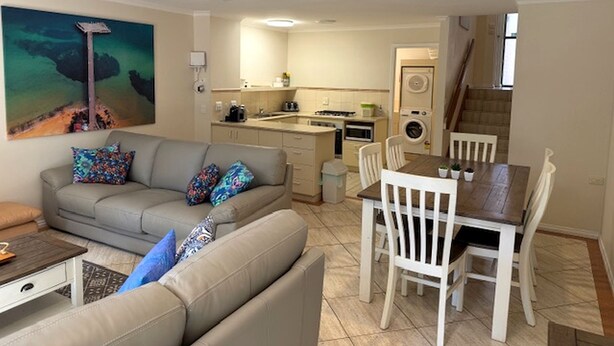 A living room with a sofa, a dining table with chairs, a kitchen area, and a staircase. - Yackataya at Cowes - Two Bedroom Villa, Sleeps 5 (Cowes)