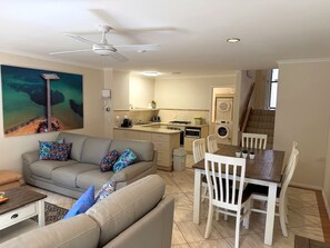 A living room with a sofa, a dining table with chairs, a kitchen area, and a staircase. - Yackataya at Cowes - Two Bedroom Villa, Sleeps 5 (Cowes)