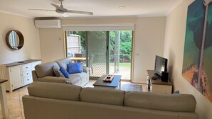A living room with a beige sofa, a coffee table, a TV, and a dining area with a white cabinet and a mirror. - Yackataya at Cowes - Two Bedroom Villa, Sleeps 5 (Cowes)
