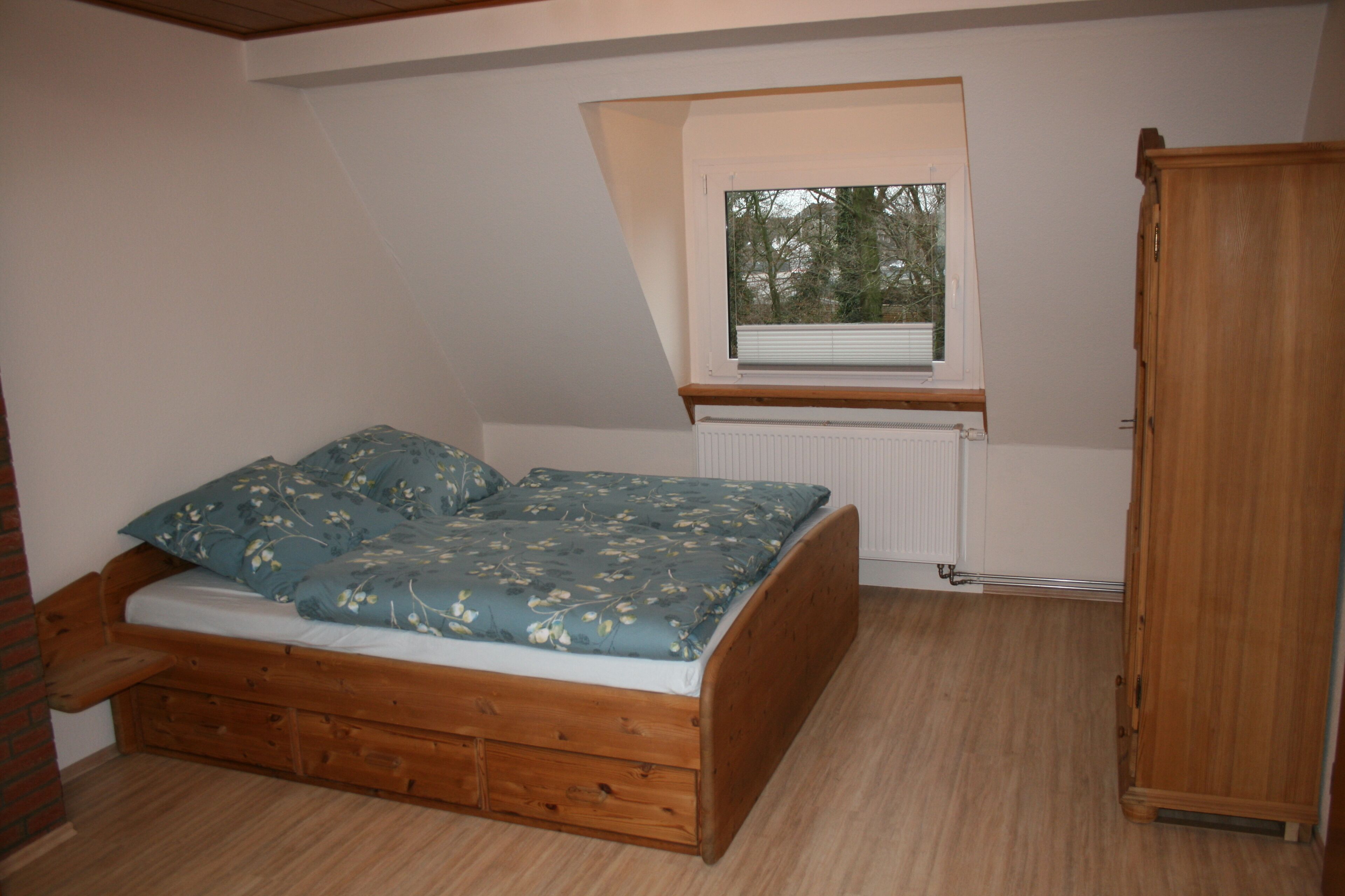 Ein kleines Schlafzimmer mit Schlafkoje, einem Fenster mit Jalousien, einem Heizkörper und einem Holzschrank.