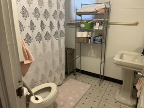 Features a white toilet, sink, and mirror, with a shelf for toiletries and a tiled floor.