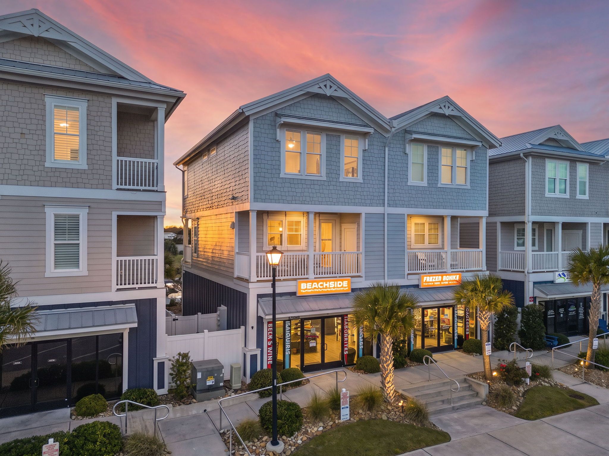 A row of two-story buildings with balconies, a beachside sign, and a frozen food store.