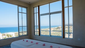 Une chambre avec un lit, de grandes fenêtres et une vue sur l’océan.