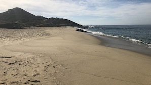 Une vaste plage de sable parsemée d’empreintes, une côte rocheuse et une montagne en arrière-plan.