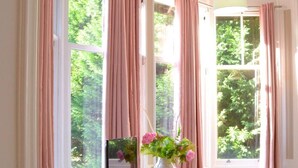 A room with a wooden desk, a television, and a bench by large windows with pink curtains. - Remarkable 1 Bed Apartment in Birmingham (Birmingham)