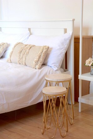 A bed with white bedding and two beige pillows, a round table with a marble top, and a wooden floor.