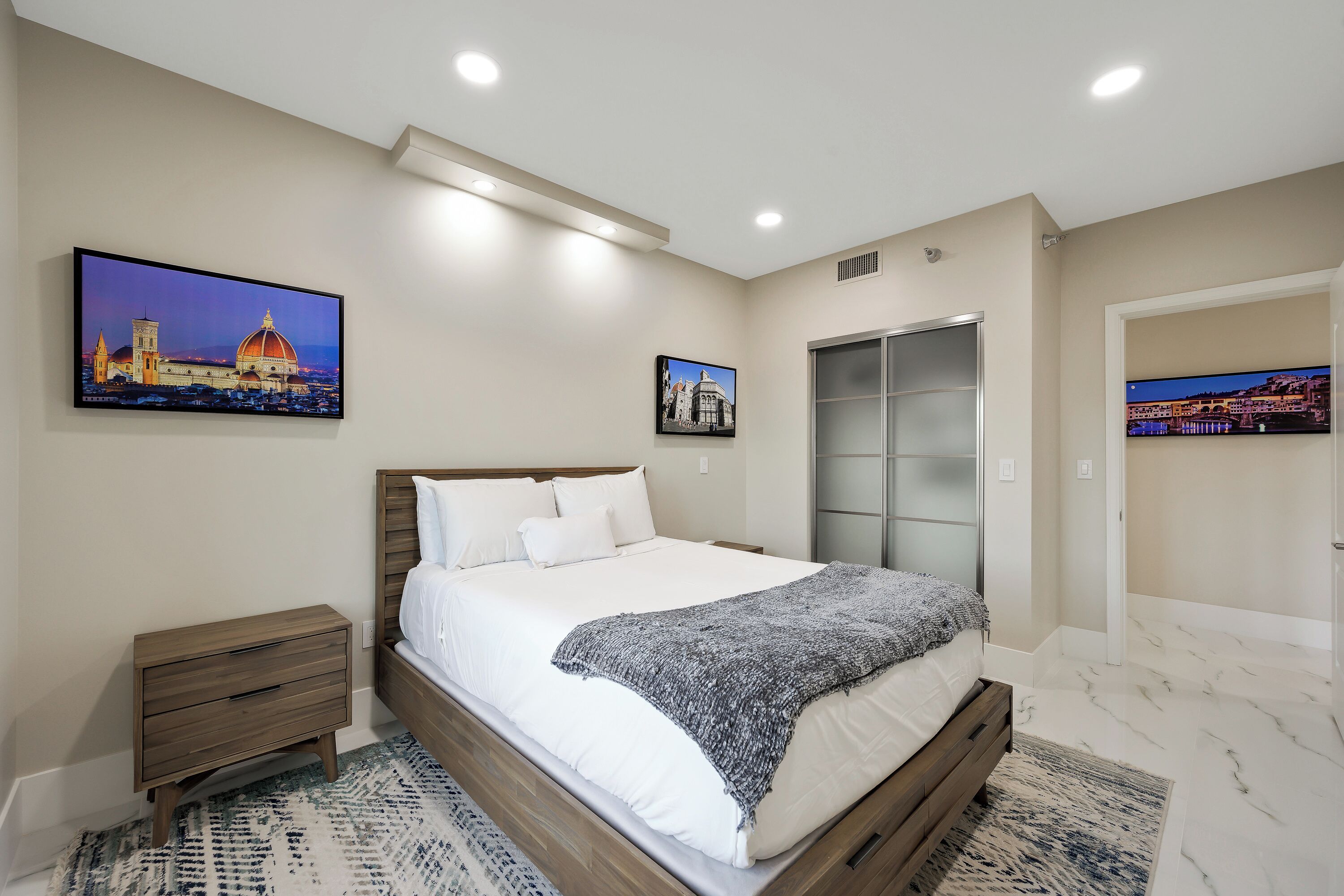 A bedroom with a large bed, a nightstand, a wardrobe, and two framed pictures on the wall.