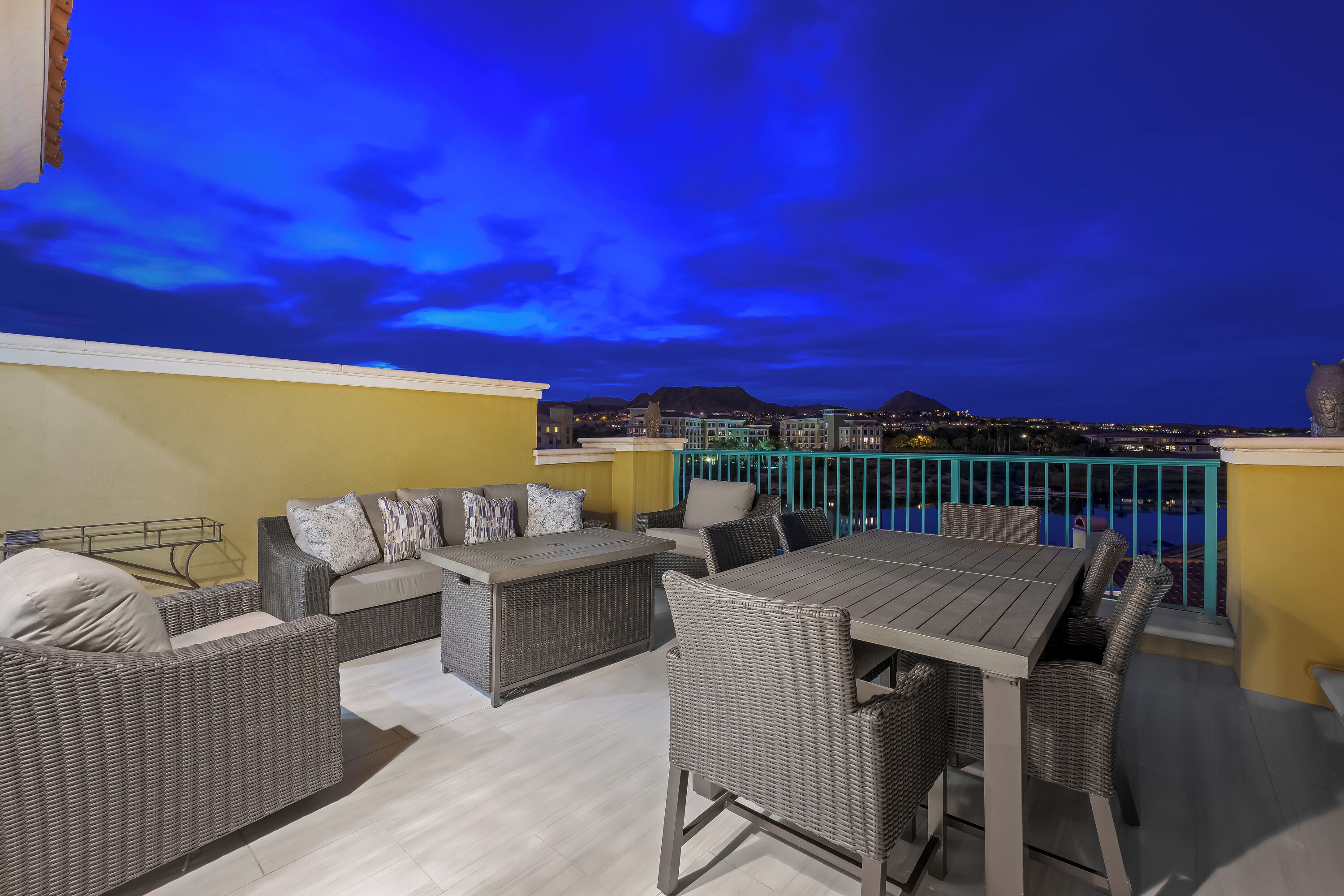 Eine Dachterrasse mit Korbmöbeln, einem Esstisch und Blick auf die städtische Skyline im Abendlicht.