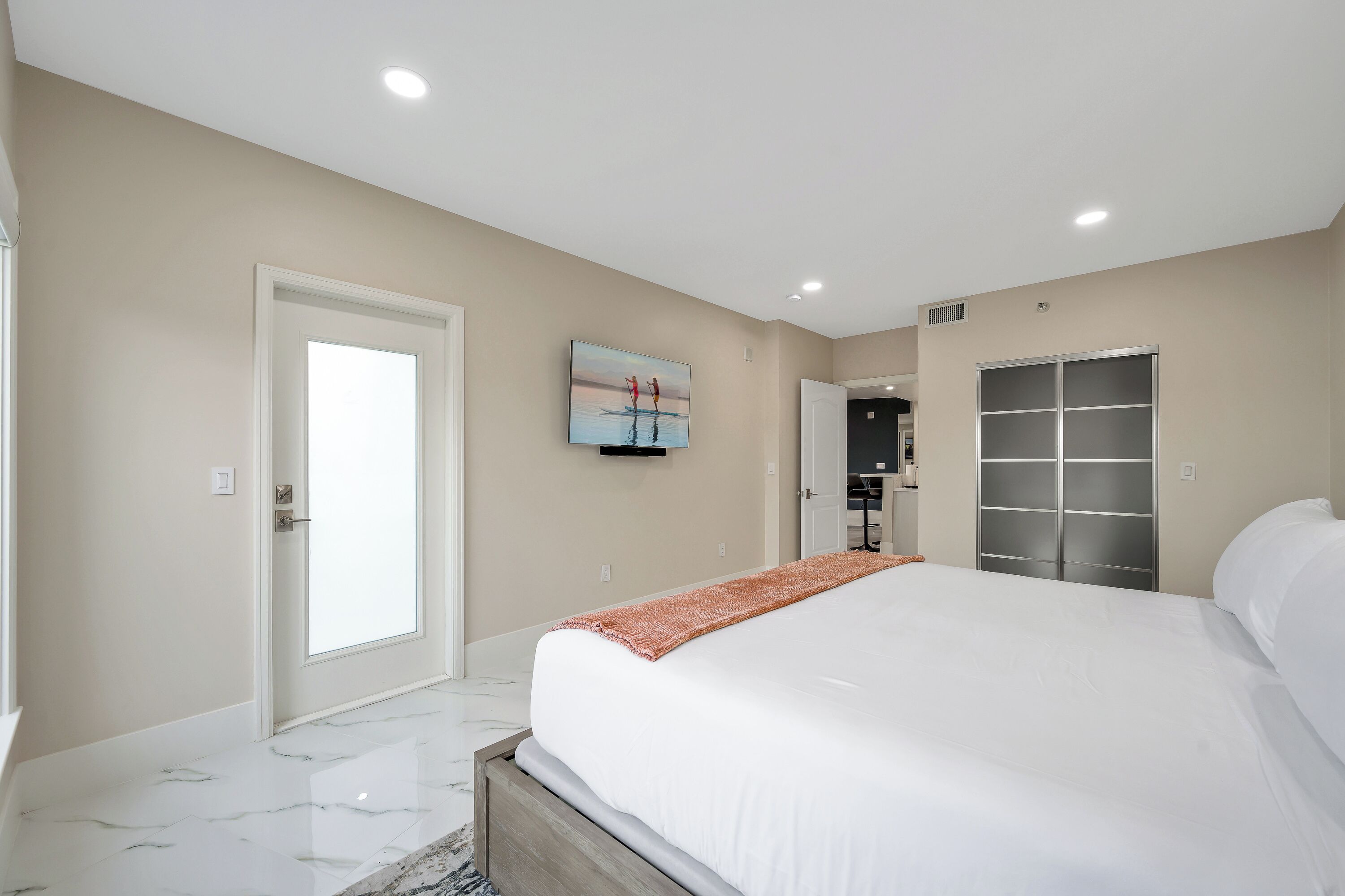 A bedroom with a large bed, a door, a wardrobe, and a painting on the wall.