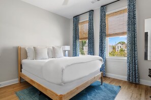 A bedroom with a bed, a window with curtains, a lamp, and a view of buildings outside.