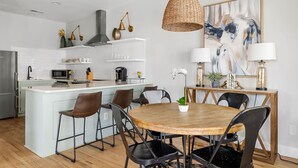 Une cuisine moderne avec des meubles blancs, un îlot central et un coin repas comprenant une table en bois et des chaises noires.
