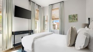 Une chambre à coucher avec un lit, un téléviseur fixé au mur, une table de chevet et une fenêtre avec des rideaux.