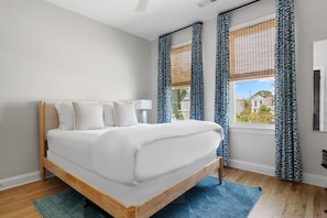 A bedroom with a bed, a window with curtains, a lamp, and a view of buildings outside.
