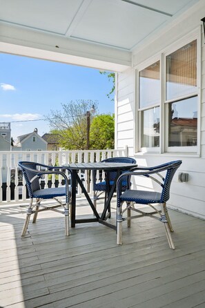 En inglasad veranda med ett bord och fyra stolar, ett vitt räcke och utsikt över de omkringliggande husen.