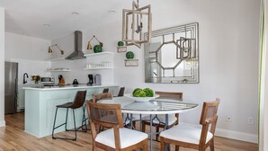 Une cuisine moderne dotée d’un îlot central, d’un coin repas avec une table ronde et des chaises, et d’un grand miroir décoratif accroché au mur.