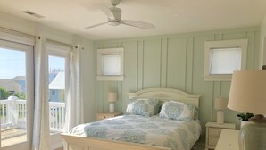 A bedroom with a bed, two bedside tables, a ceiling fan, and a view of the outside. - Spacious and Bright townhome, steps to the beach, pet friendly* (Carolina Beach)