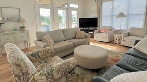 A living room with a sofa, ottoman, and a television. - Spacious and Bright townhome, steps to the beach, pet friendly* (Carolina Beach)