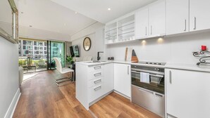 A modern kitchen with white cabinetry, a built-in oven, and a dining area with a chair and table.