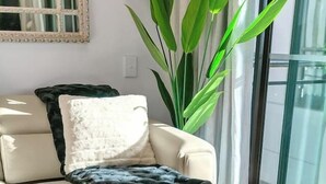 A modern living room with a sofa, a glass coffee table, and a large plant.