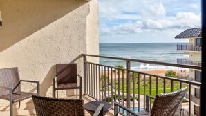 Ein Balkon mit Korbmöbeln, der Blick auf Strand und Meer bietet.