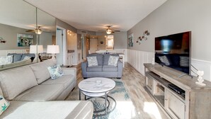 Ein geräumiges Wohnzimmer mit einem grauen Sofa, einem runden Couchtisch und einem Fernseher auf einem Holzgestell.