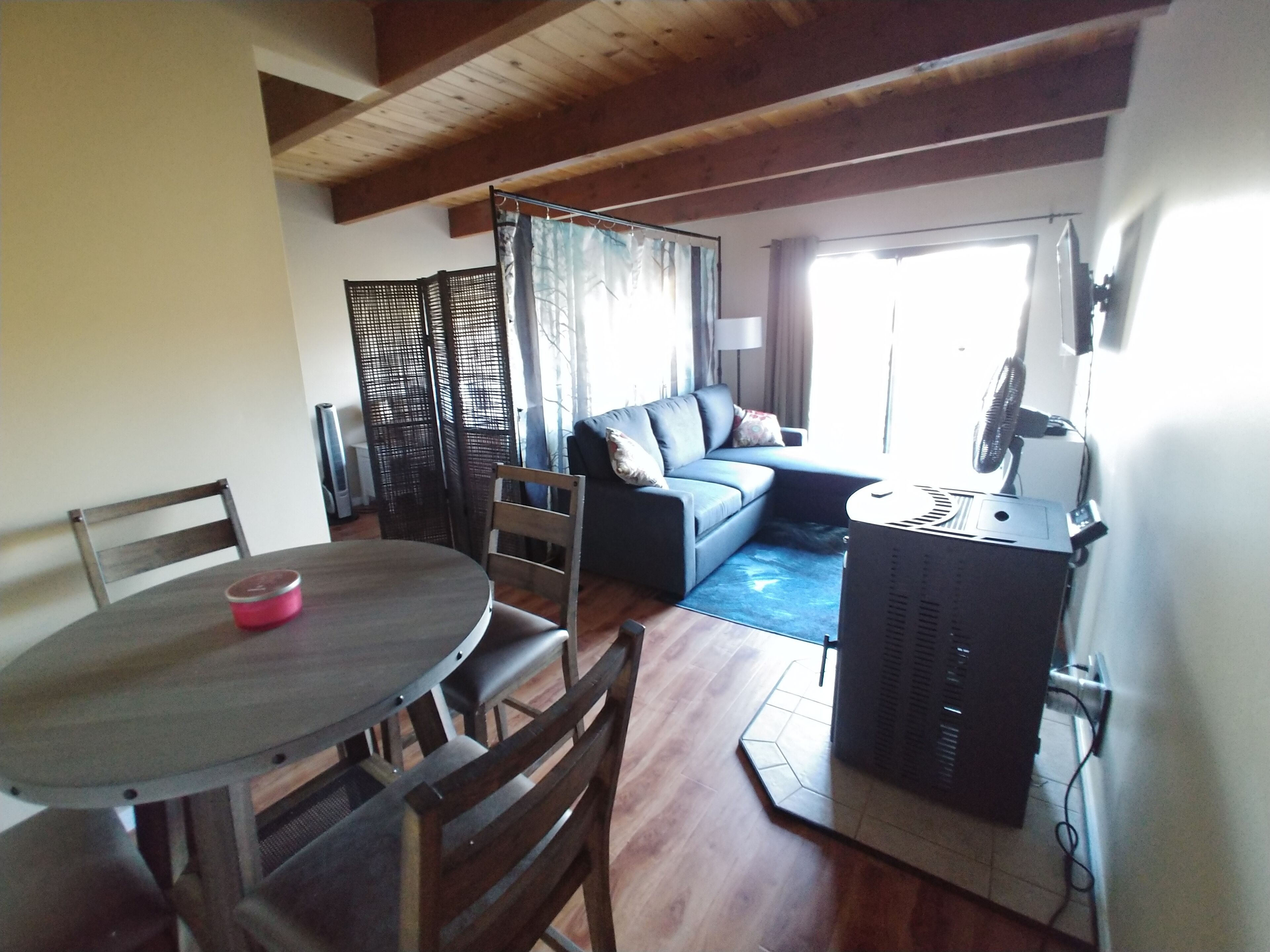 A living room with a sofa, a dining table with chairs, a heater, and a window with curtains.