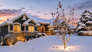 Une maison recouverte de neige, avec une façade en briques, un toit à pignon et une entrée bien éclairée.