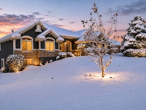 Une maison recouverte de neige, avec une façade en briques, un toit à pignon et une entrée bien éclairée.