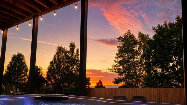 Banheira de hidromassagem com vista para o pôr do sol, deck de madeira e cadeiras.