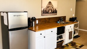 A compact kitchen with a stainless steel refrigerator, white cabinetry, a wooden countertop, and a patterned rug.
