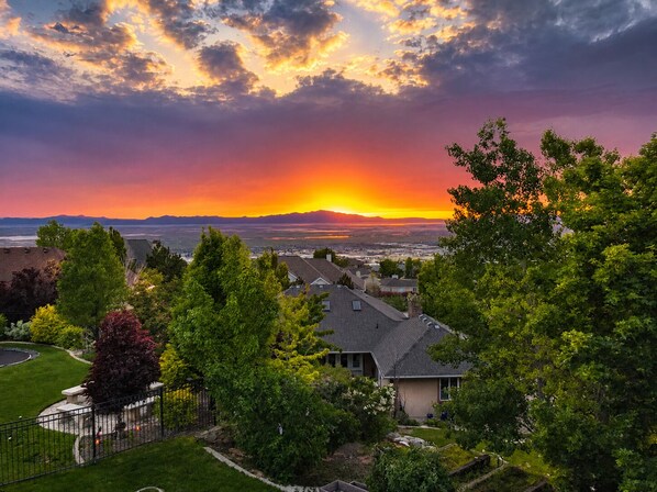 Un barrio residencial con casas, un césped cuidado y vistas de un atardecer sobre un paisaje lejano.