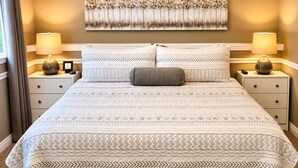 Un lit bien fait, avec une couvre-lit à motifs et des oreillers, de part et d’autre duquel se trouvent des tables de chevet avec des lampes et un tableau encadré.