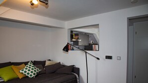 Una sala de estar moderna con un sofá marrón oscuro, una lámpara de pie y un ventanal sobre una zona de cocina.