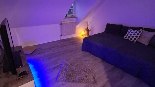 Un dormitorio acogedor en el ático, con techo inclinado, piso de madera, un sofá azul y un televisor sobre un mueble.