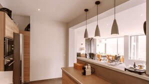 A modern kitchen with wooden cabinets, a built-in oven, and a long countertop. There are pendant lights above the counter and a window providing natural light. - Experience the Exception at Chalet La Source: Comfort, Relaxation and Magnificent Views (Cauterets)