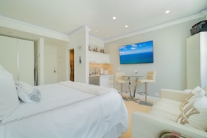A hotel room with a bed, a sofa, a small dining table, a TV, and a kitchen area.