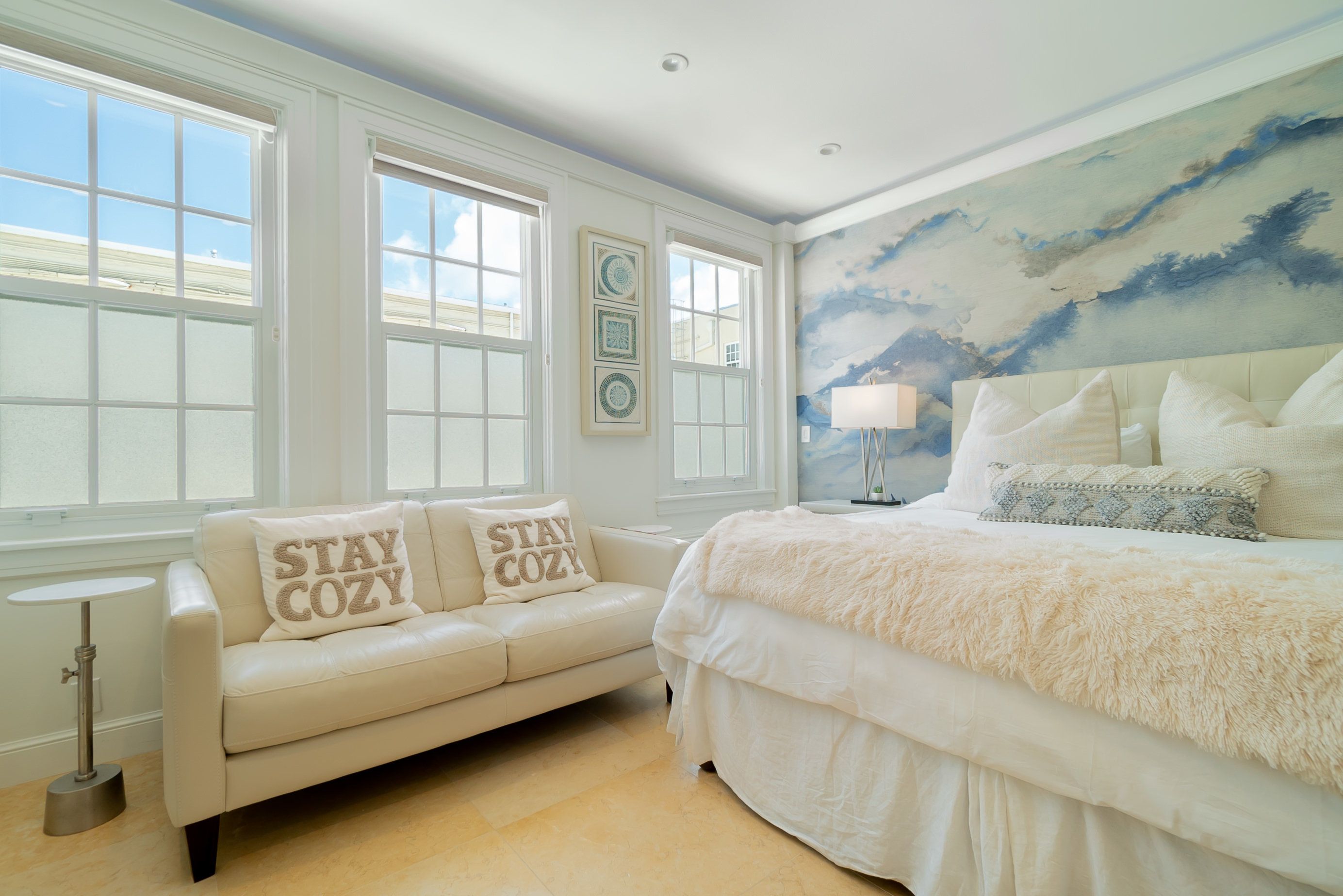 Un dormitorio con una cama grande, un sofá con dos almohadas, una mesita y una pared decorada con cuadros.