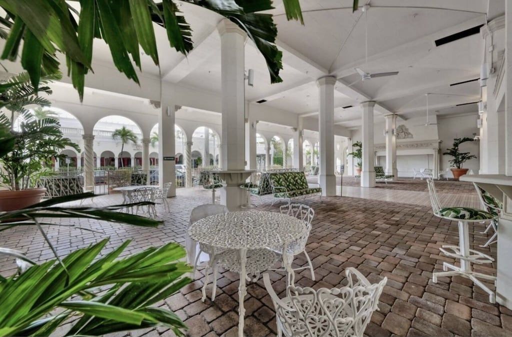 Un amplio patio con columnas blancas, una mesa redonda en el centro y sillas blancas alrededor.