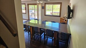 A dining area with a glass-top table and chairs, a ceiling fan, and a view of the outdoors through large windows. - Sleeps 18!  Heated pool and lake access. (Mears)