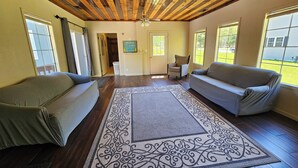 A spacious room with wooden ceiling beams, two sofas, a patterned rug, and large windows offering a view of the outdoors. - Sleeps 18!  Heated pool and lake access. (Mears)