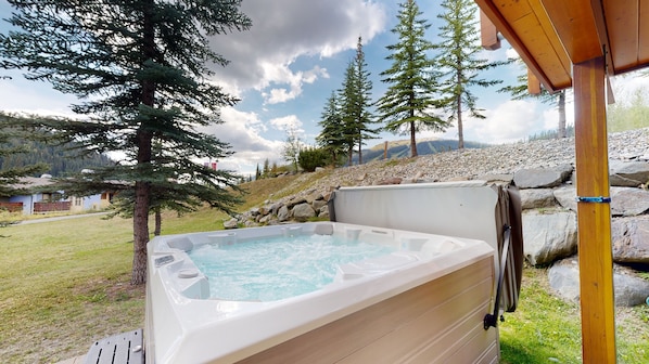 A hot tub in a natural setting with trees and a mountainous background. - Trail's Edge #1 | 3 Peaks Rentals (Sun Peaks)