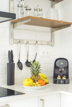 A kitchen with a fruit bowl on the counter, a coffee maker, and utensils hanging on the wall.