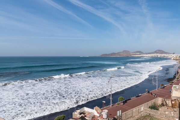 A coastal view with a beach, waves, and a distant mountain range.
