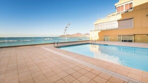 Una piscina con vistas al océano, un solárium con baldosas y un edificio con grandes ventanales.