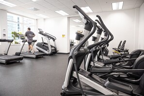 A gym with multiple treadmills, a person using one, and a window with a city view. - Cozy Brickell Studio with FREE parking and Pool, Game Room and Jacuzzi (Miami)