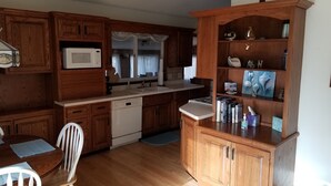 A kitchen with wooden cabinets, a microwave, a dishwasher, and a dining area with a table and chairs. - Lake Access! 5 minutes to the dunes! (Mears)