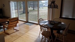 A dining area with a wooden table and chairs, a ceiling fan, and a view of the outdoors through large sliding glass doors. - Lake Access! 5 minutes to the dunes! (Mears)