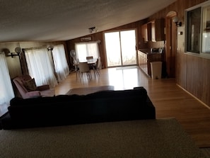 A spacious living area with a large sofa, a dining table with chairs, and a kitchen area with wooden cabinets and a window.