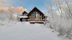A log cabin with a wooden deck and large windows, surrounded by snow-covered trees. - Luxurious Mountain Retreat - Minutes from Park City and Deer Valley (Coalville)